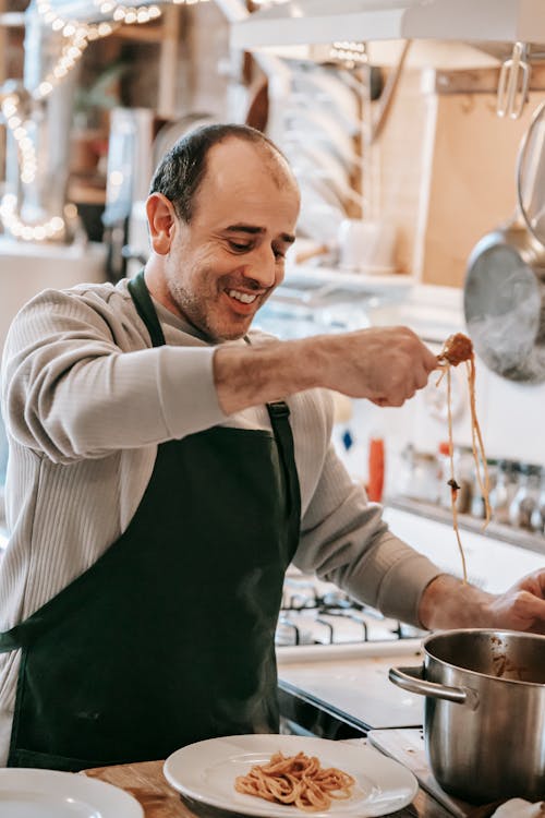 Delighted ethnic man serving delicious spaghetti during dinner at home