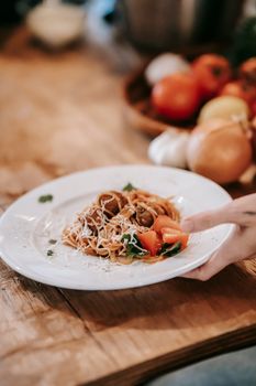 From above of crop anonymous female serving plate of delicious spaghetti with meatballs and vegetables on wooden table in kitchen