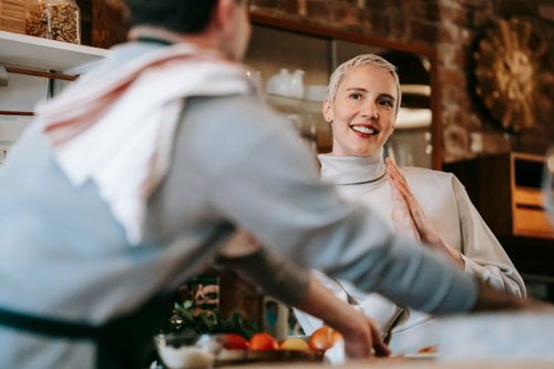 Free Positive adult couple in bright kitchen while male cooking meal on counter with various ingredients and products near female friend while looking at each other Stock Photo