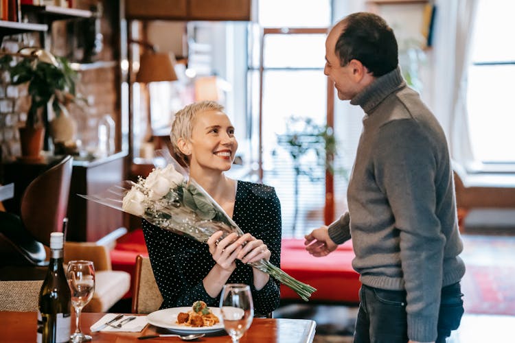 Smiling Couple Having Date In Restaurant With Bouquet And Food