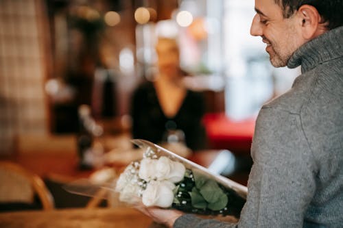 Couple having date in restaurant with man with flowers bouquet