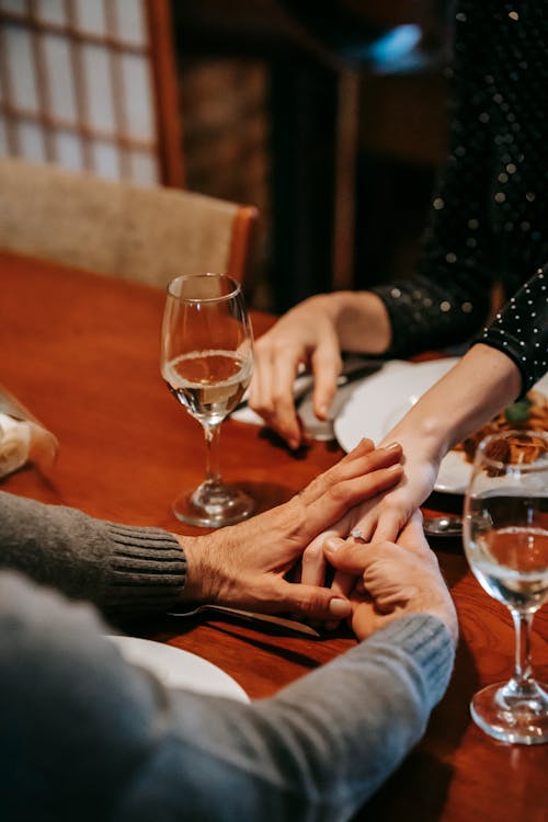 Free Crop unrecognizable couple holding hands while having date at table with glasses with wine near plates with food in bright room Stock Photo