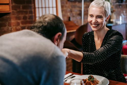 Free Smiling couple having date while man kissing woman in hand at table with wineglass and plates with pasta with meatballs near cutlery in light restaurant Stock Photo
