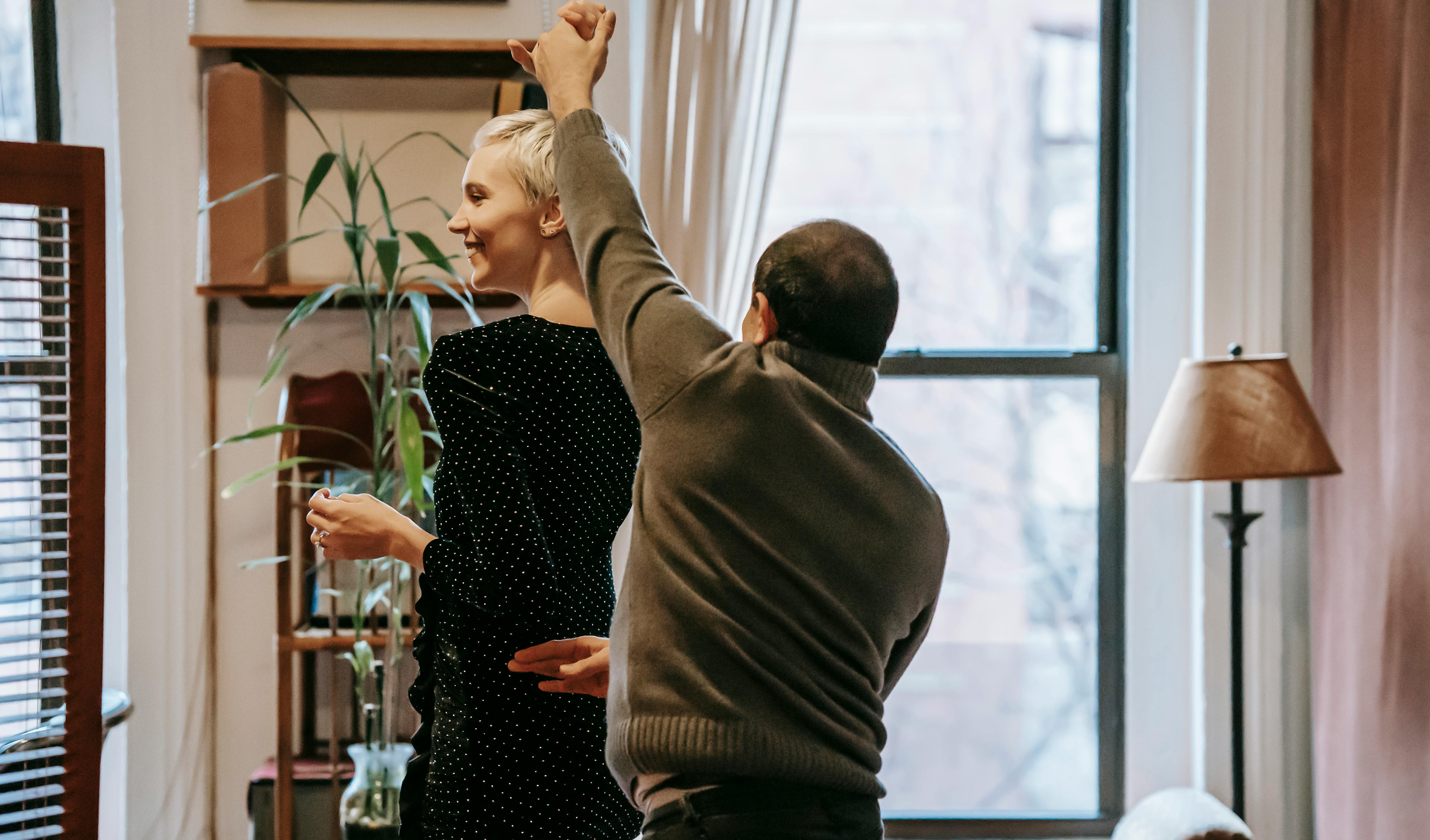 smiling couple dancing in room near window