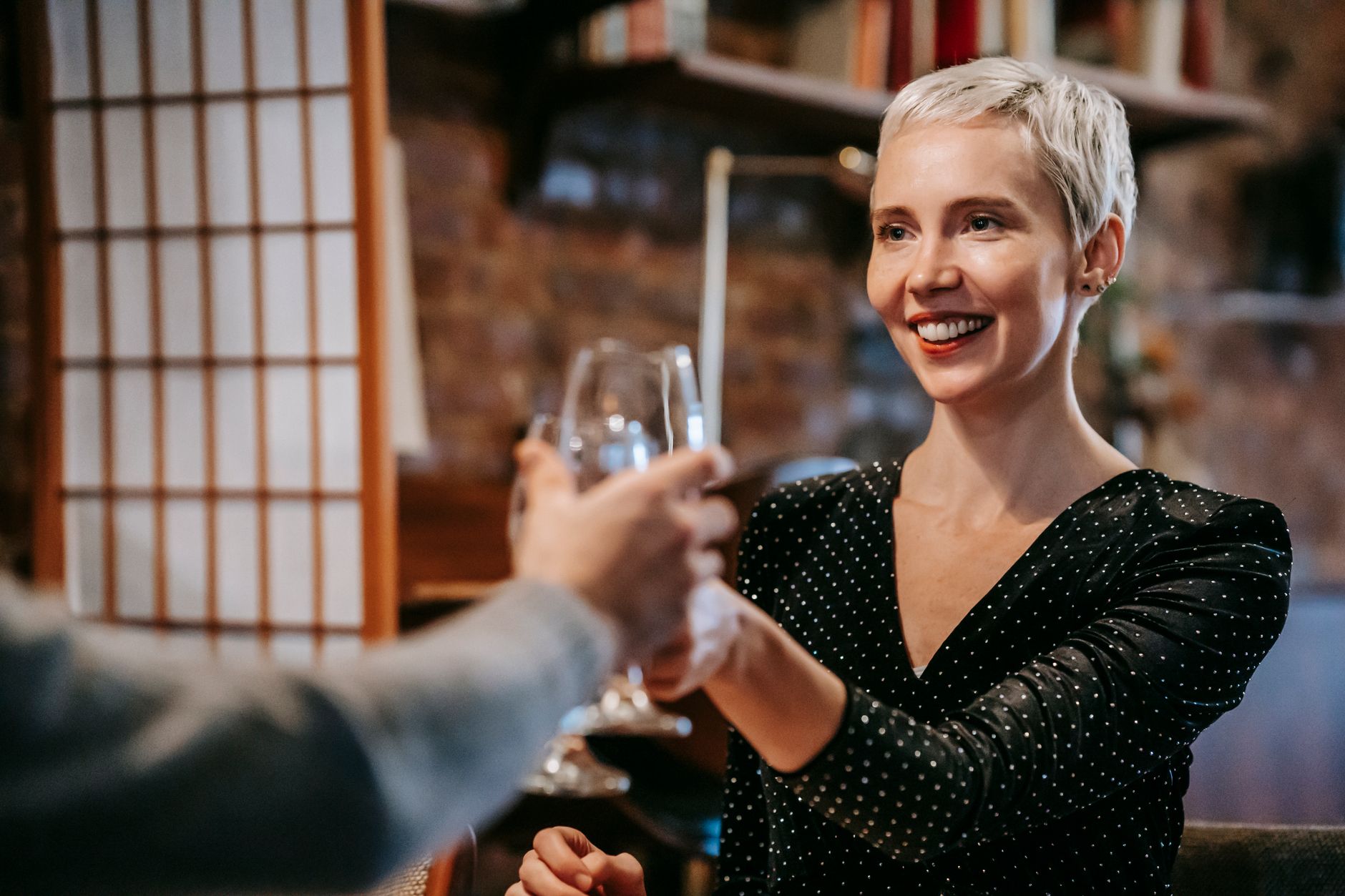 Smiling couple sitting in light room while having dinner and clinking glasses with wine