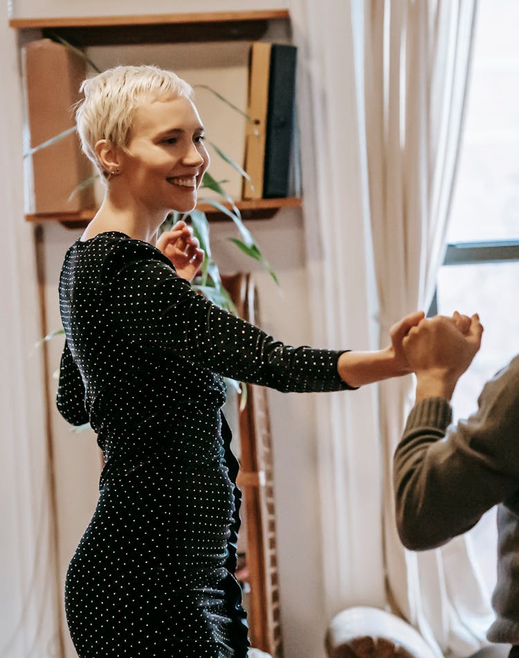 Positive Couple Dancing While Holding Hands In Apartment Near Window