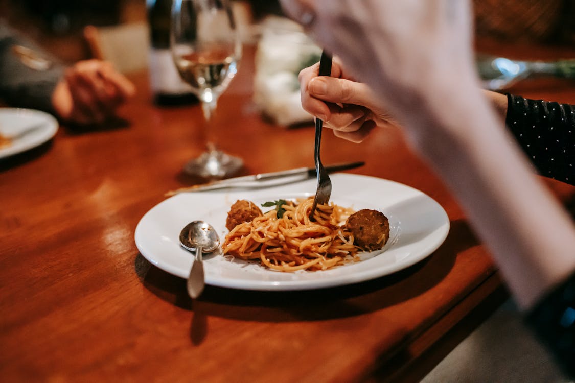 Free Crop anonymous female enjoying tasty yummy spaghetti with meat ball and glass of white wine in restaurant Stock Photo