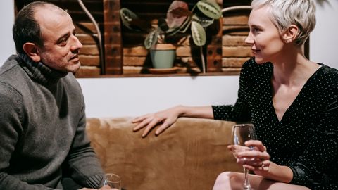 Side view of couple sitting on sofa with glasses of drink and having conversation