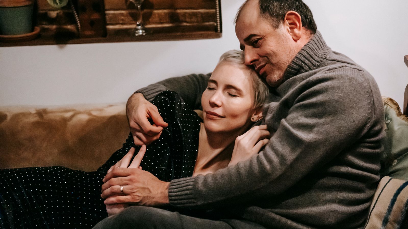 Two adults sitting close and holding hands on a sofa