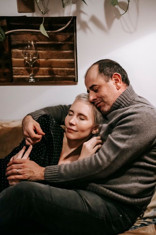 Free Affectionate adult couple embracing with closed eyes and holding hands on couch under plant Stock Photo