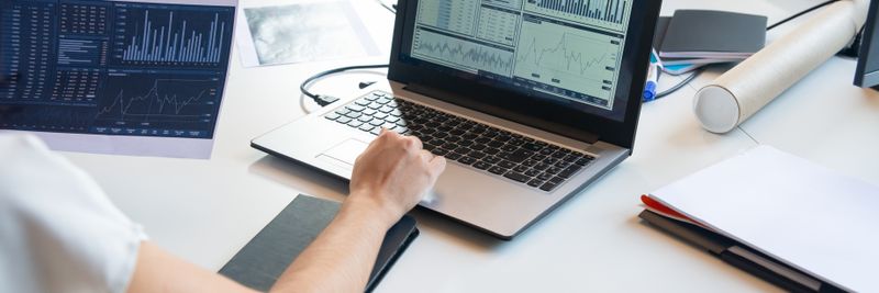 Business person evaluating financial charts on a laptop in a modern office setting.
