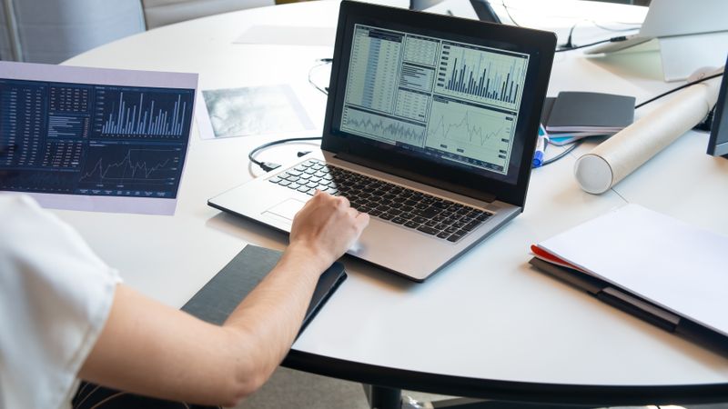 Business person evaluating financial charts on a laptop in a modern office setting.