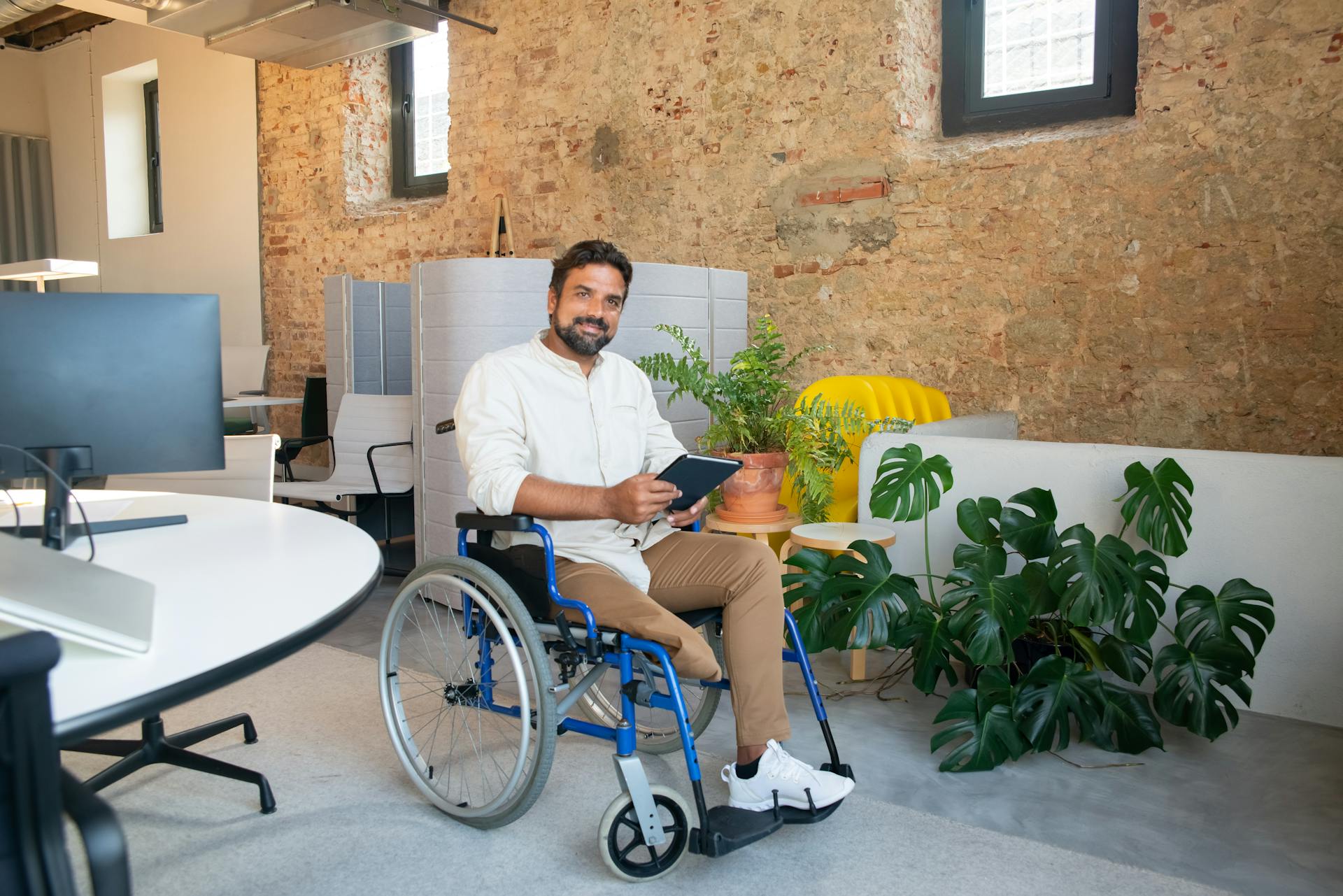 Businessman in wheelchair holding tablet device in modern office setting.