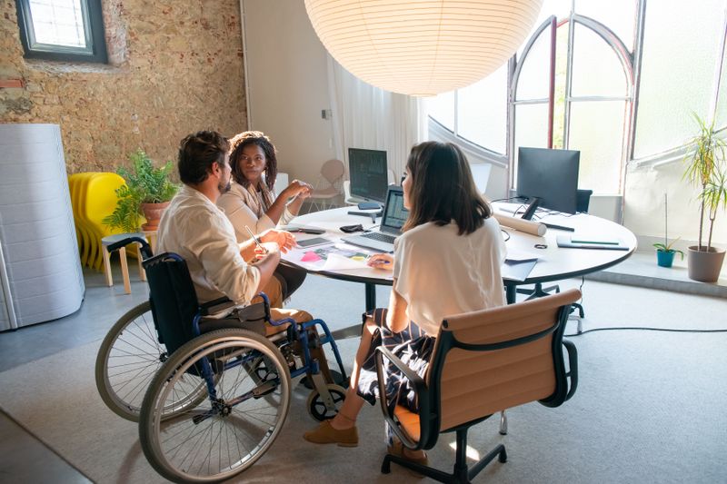 An inclusive team meeting in an office setting with individuals of diverse abilities collaborating.