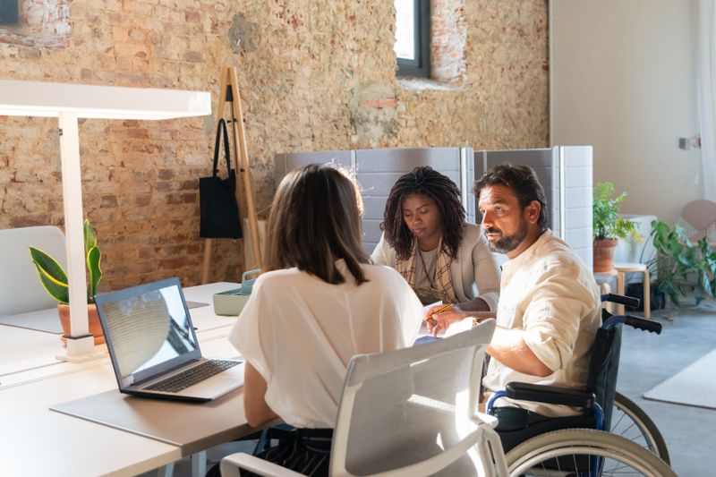 A diverse team working together in an office, including a person in a wheelchair and a person with a service animal.