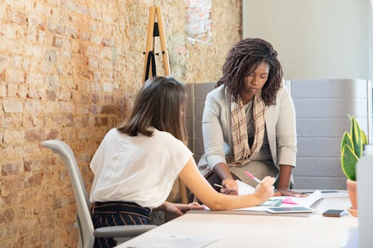 Two women collaborating on a project in a modern office with a stylish brick wall.