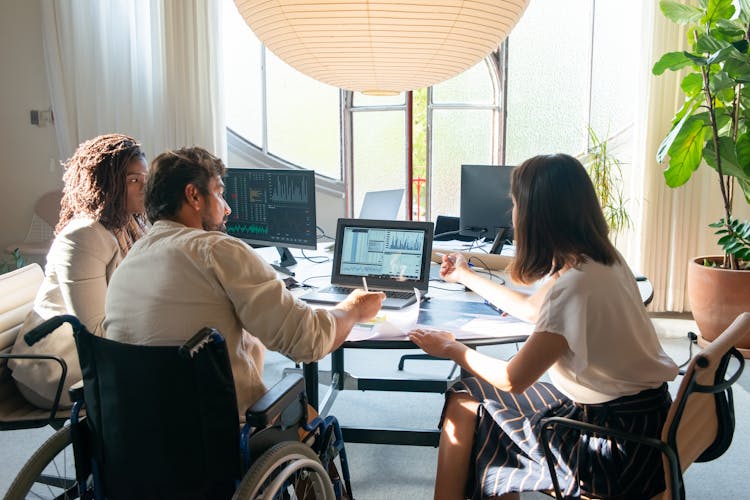 Photograph Of Colleagues Talking Near A Laptop With Charts