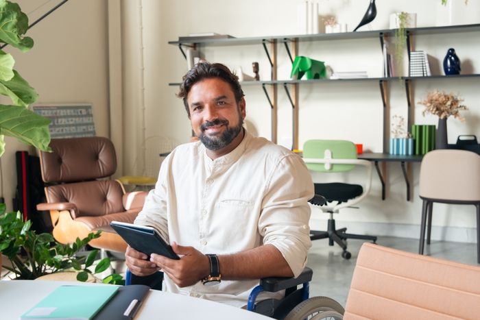 Bearded man in a wheelchair using a tablet and smiling indoors