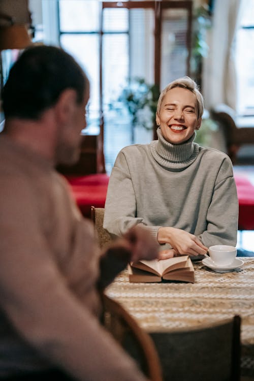 Laughing woman at table with book and cup of drink