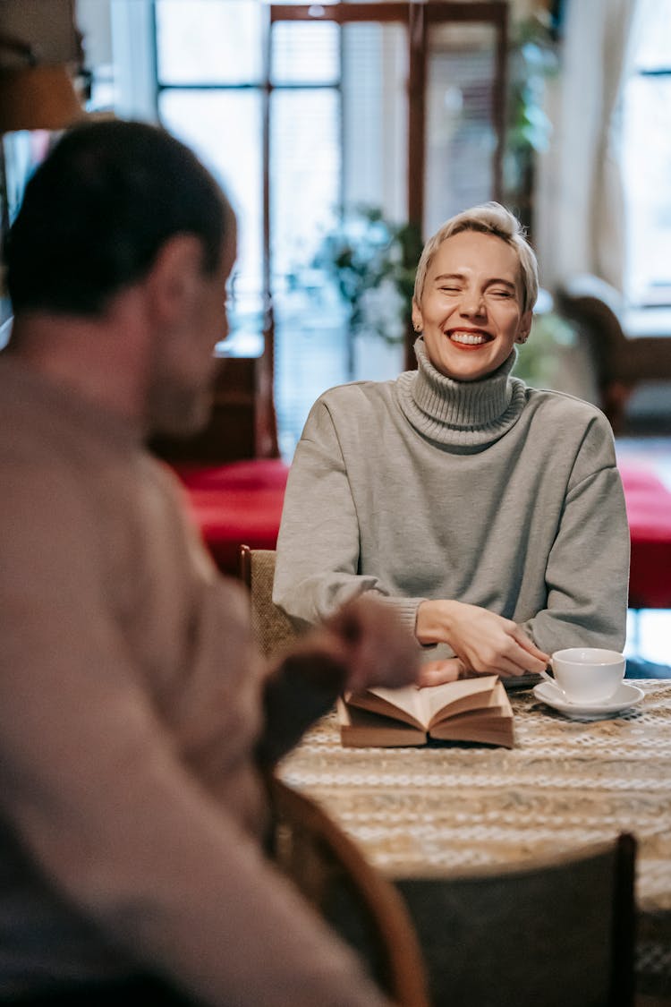 Laughing Woman At Table With Book And Cup Of Drink