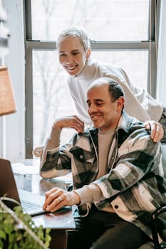 Smiling couple collaborating on a laptop in a cozy indoor setting, embracing teamwork.