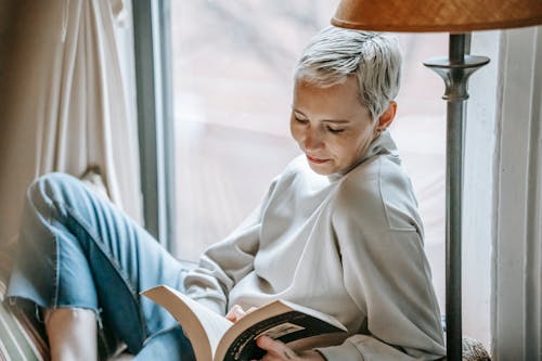 Woman reading book sitting on windowsill