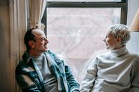 Positive couple in casual clothes sitting near window and enjoying weekend together at home
