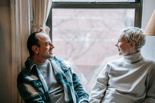 Free Positive couple in casual clothes sitting near window and enjoying weekend together at home Stock Photo