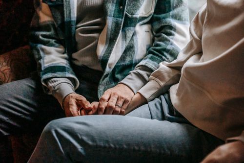 Free Unrecognizable tender couple in casual wear and warm shirts sitting on comfortable couch while holding hands in room at home Stock Photo