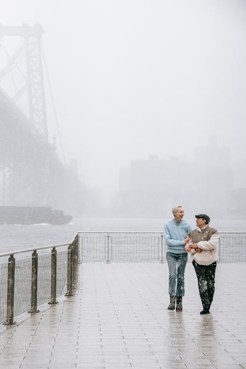Couple walking on embankment near river and bridge in winter