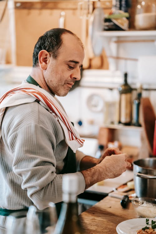 Thoughtful man in apron cooking dish on counter in kitchen