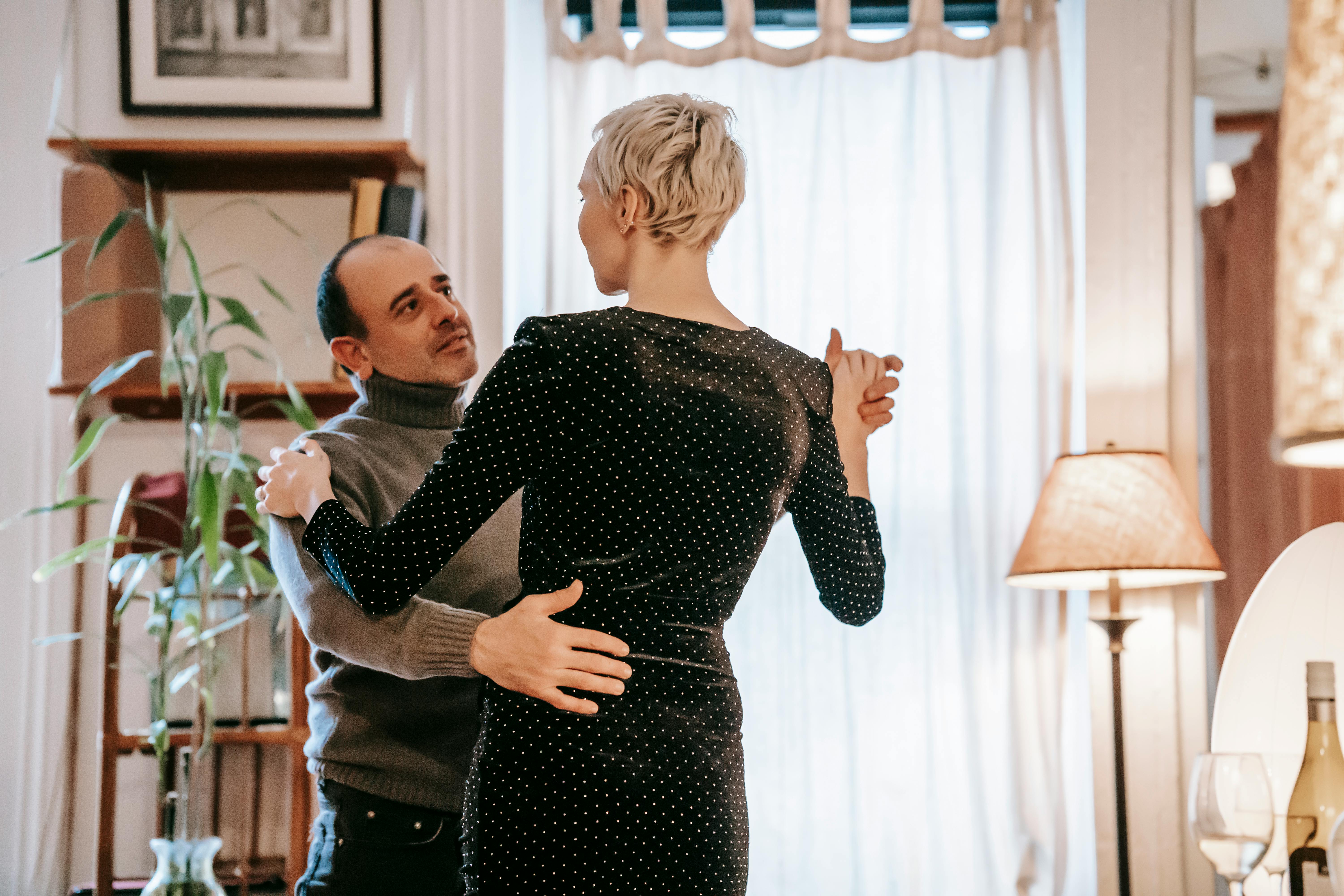 Romantic adult couple holding hands while dancing in room and enjoying pleasant time together