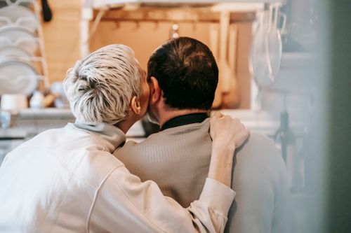 Free Back view of unrecognizable couple sitting closely while cuddling and caressing cheeks gently in kitchen Stock Photo