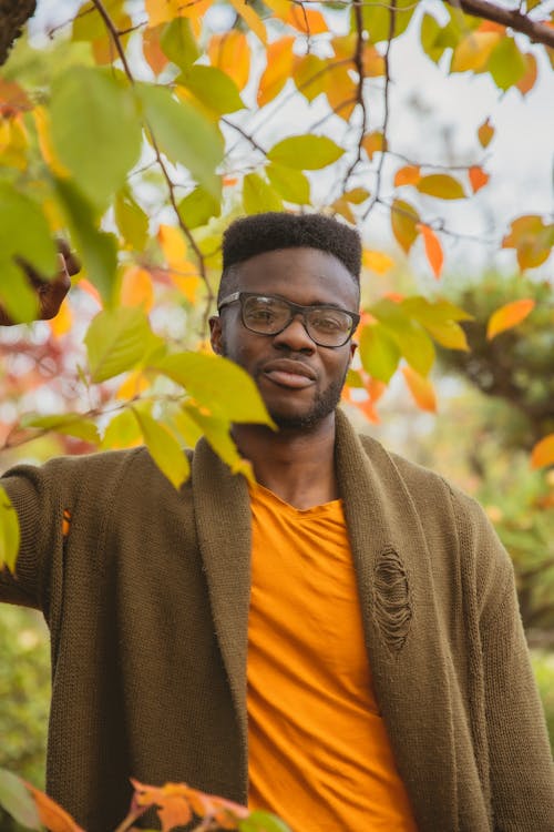 Content young black man resting near tree in autumn garden