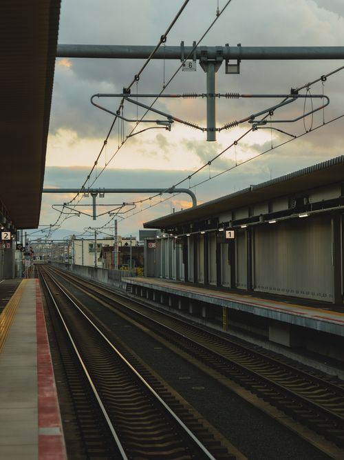 Free Empty railway platform with metal rails and power lines against cloudy sky on street in city with buildings in distance Stock Photo