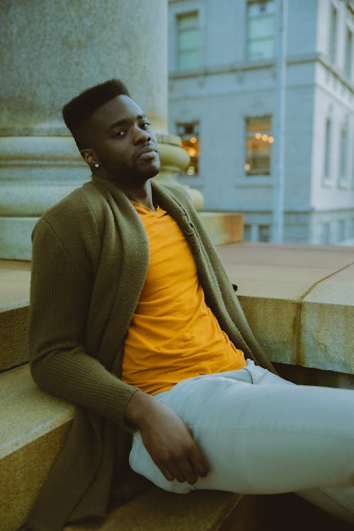 Stylish black man sitting on step near column