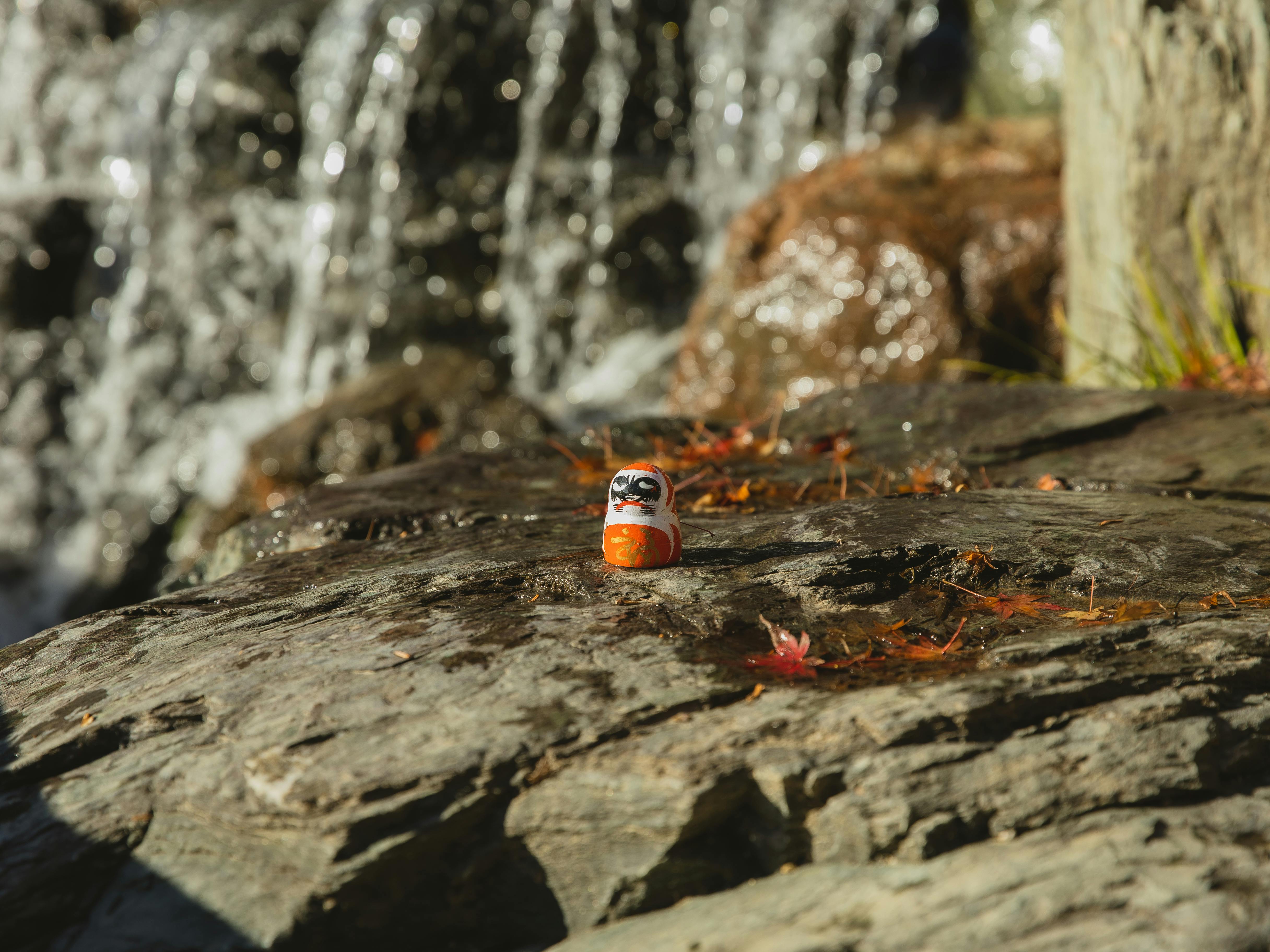 daruma doll on rocky formation near waterfall