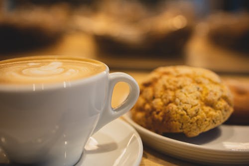 Mug of tasty fragrant coffee with latte art served near plate with oatmeal cookies on table on blurred background