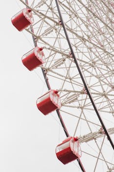 A striking image of a Ferris wheel's red cabins against a pale sky, highlighting geometry and engineering.