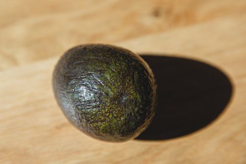 Free High angle of healthy avocado with dark green peel placed on wooden table in daylight Stock Photo