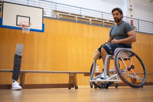 Adult man in wheelchair with prosthetic leg at indoor basketball court preparing for practice.