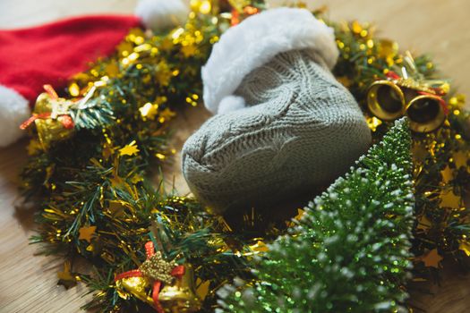 From above of knitted gray booties placed near wreath on wooden table with Santa hat and decorative fir during holiday celebration at home