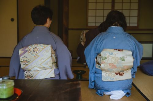 Free Back view of anonymous people in authentic robes sitting on tatami with tenmoku tea bowl during traditional Japanese ceremony in room Stock Photo