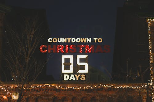 Illuminated countdown to Christmas showing 5 days on signboard placed on roof of building on dark street during holiday