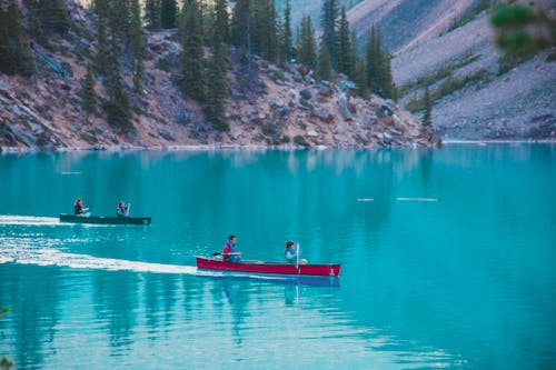 Distant people in canoes on calm turquoise river surrounded by steep cliffs with green trees during trip in nature