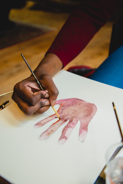 From above of anonymous African American male painter with brush drawing palm of head while sitting at table on blurred background