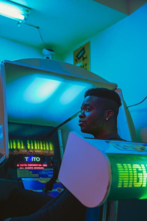Free Side view of young African American man looking away against entertainment machine in building with shiny light Stock Photo