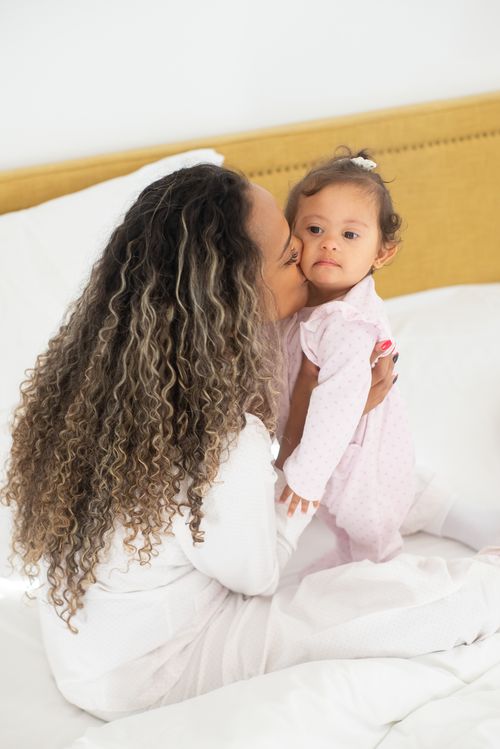 Free A loving mother gently kisses her baby while sitting on a cozy bed in a bright room, embracing affection and family bonds. Stock Photo