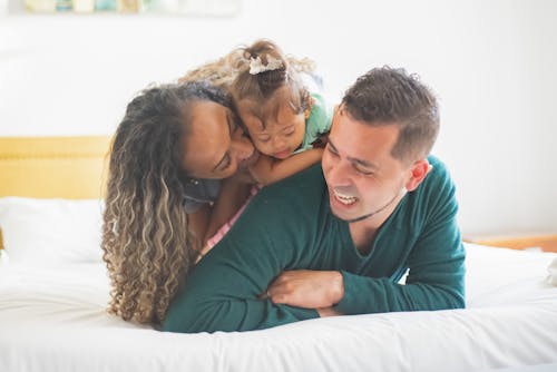 Photograph of a Family Smiling on a White Bed