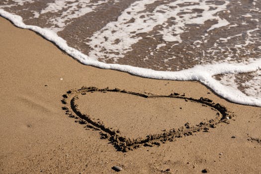 A heart shape drawn on a sandy beach as waves gently approach, symbolizing love and tranquility.